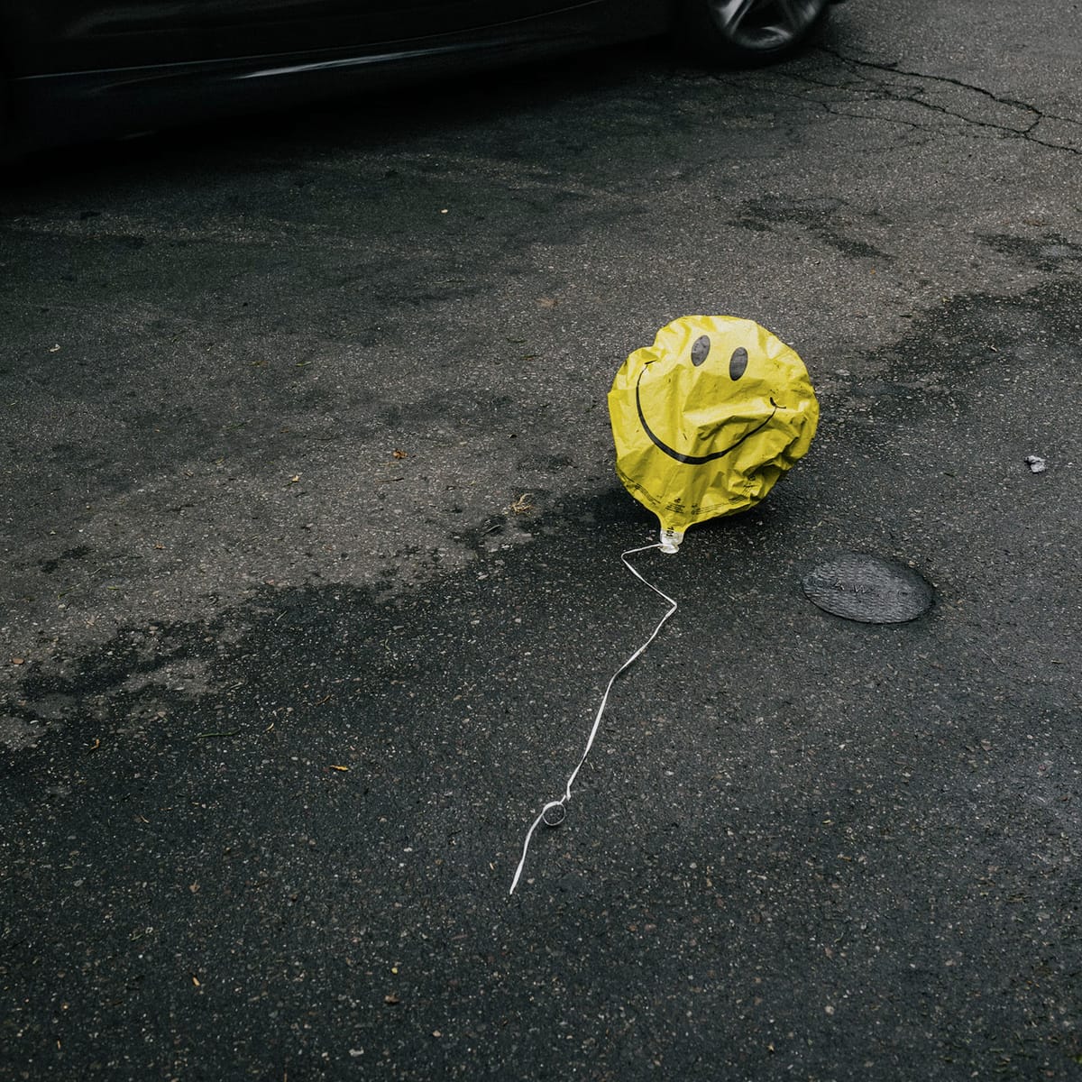 Deflated smiling emoji balloon on a road.